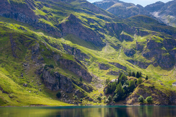 Fototapeta na wymiar Mountain lake in the middle of the alps. Summer in the green mountain with a blue lake. Alpine mountains with a play of light and shadow of the clouds.