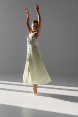 Pretty ballerina in dress spinning on grey background with sunlight