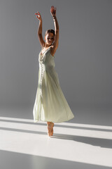 Fototapeta premium Pretty ballerina in dress spinning on grey background with sunlight