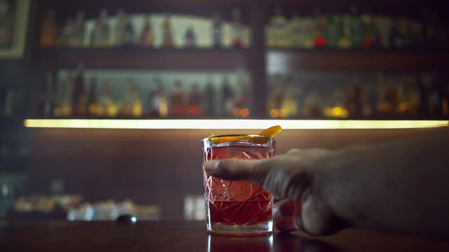 Bartender serves the visitor a red cocktail with an orange - negroni, the hand takes a glass.