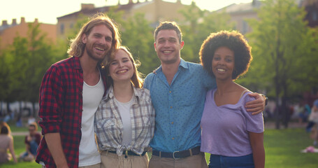 Obraz premium Medium shot of positive multiracial young friends having fun at park hugging and smiling at camera