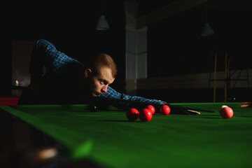 Young handsome man leaning over the table while playing snooker