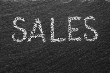 Sales whritten with white chalk on black stone texture. Macro texture text. 