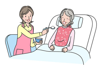 ベッドでシニア女性の食事介助をする中高年の女性