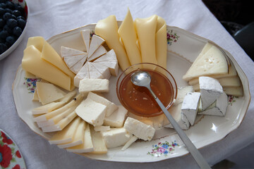 There are different types of cheese on the plate. In the center is a saucer with honey.