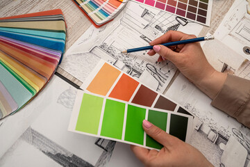 Female interior designer chooses color from the palette, working with house sketch