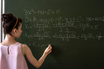 schoolgirl writing high school maths formula  with chalk on blackboard