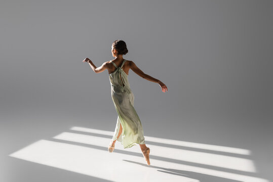 Elegant ballerina dancing and jumping on grey background with sunlight