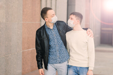 Young gay couple wearing medical mask, hugging and kissing at the city.