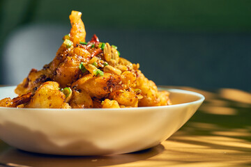 Chicken in sweet and sour sauce, with Sichuan pepper, peanuts in a white bowl. Wood background. Chinese cuisine