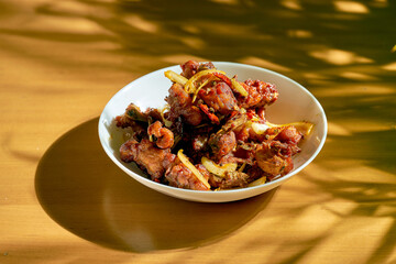 Fried chicken in chili sauce with onions in a white plate. Wood background. Chinese cuisine