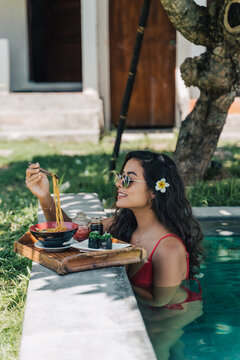 Smiling tourist with tasty noodles in pool during trip