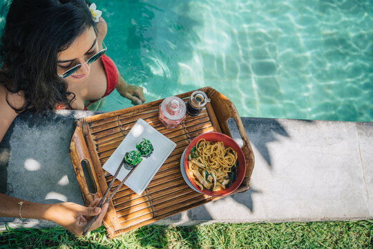 Crop traveler with delicious sushi rolls on poolside in resort