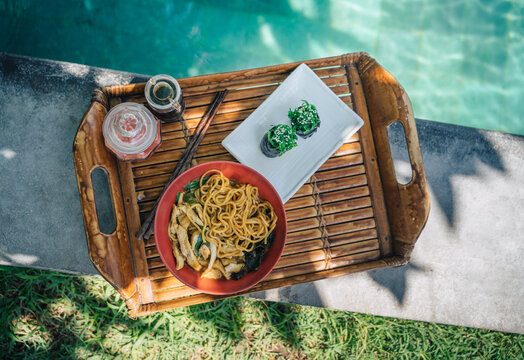 Delicious sushi and bowl of noodles with chicken slices outdoors