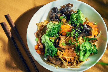 Wok noodles with beef, vegetables, sweet and sour sauce and Sichuan pepper. Wood background. Chinese cuisine