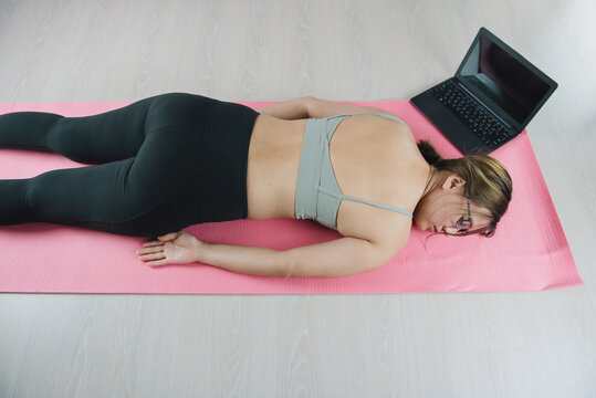 Tired after exercise and workout. Overtraining concept. Exhausted young asian woman lying on floor and resting after heavy online training in home gym at yoga mat.