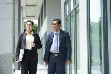 Smiling senior businessman and businesswoman walking along the street of city downtown