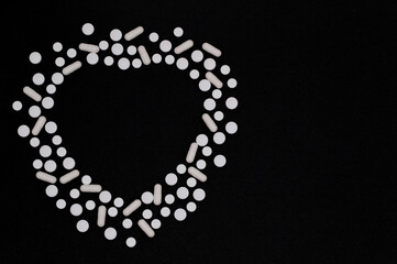 White pills and capsules of medicines are spread out on a black background in the form of heart, the concept of medicine and pharmacy, top view