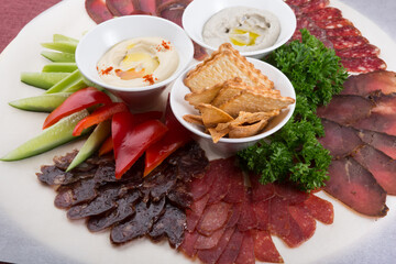 Plate of assorted sliced salted and dried meat served with humus