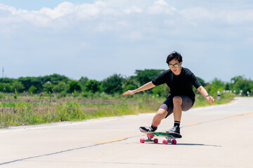 Fototapeta premium A young Asian man in a black shirt and pants is playing figure skating on a rural road. in the sun on a bright day, Play surf skate.