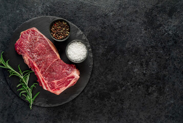 Raw marbled beef New York steak with spices on a stone background with copy space for your text	