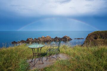 Fototapeta na wymiar Wonderful seaside view with empty table and chair near the beach and a rainbow over the sea