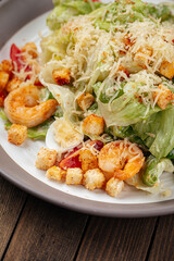 Caesar salad with shrimp and croutons on wooden background