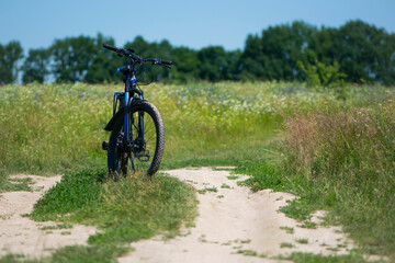 Fototapeta na wymiar bike stands on the road in the field. A mountain bike stands on a field path with green grass. Mountain bike, blooming summer field, meadow flowers, sunny day. ride a bike. outdoor activities