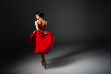 Side view of ballerina dancing and holding red dress on black background