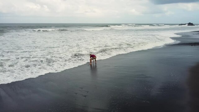 Man walking on black sand Bailan beach in Bali before storm. High quality 4k aerial footage
