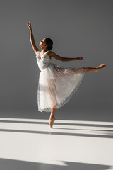 Side view of elegant ballerina dancing on grey background with sunlight