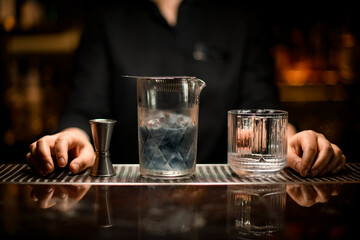 Close-up of mixing cup with cold cocktail and old-fashioned glass and jigger on the bar