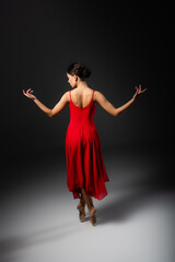 Naklejka premium Side view of ballerina in red dress looking away on black background