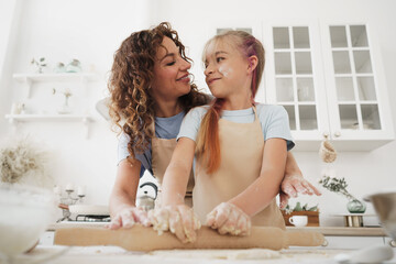 Teen girl helping her mom to cook dough in their kitchen at home