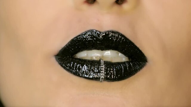 Closeup of a beautiful woman lips with beautiful black makeup and piercing sending air kiss . Close up of girl's mouth having flirty emotions and sending air kiss 