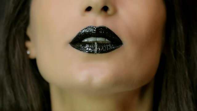 Closeup of a beautiful woman lips with beautiful black makeup and piercing sending air kiss . Close up of girl's mouth having flirty emotions and sending air kiss 