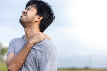 Asian man suffering from shoulder pain outdoors