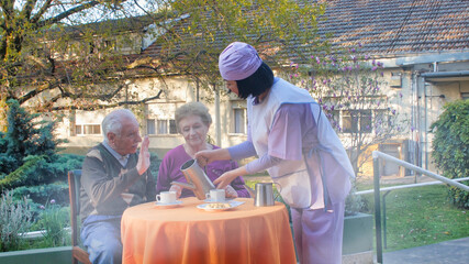 Young asian waitress serving breakfast to elderly retired couple in a hospital rehab garden