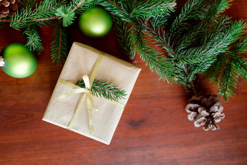 Christmas gift box with Christmas tree branch decor and gold ribbon on a wooden brown background. Christmas balls and cones. copy space. Recycled paper has been used.