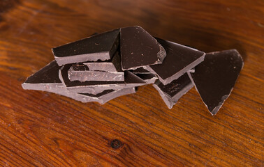 Broken pieces of dark chocolate on a wooden brown background.	