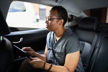 African woman sitting in back seat of the car and working online using digital tablet