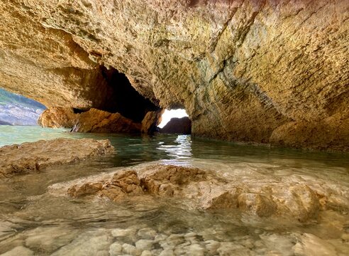 Cave in sea. Sea cave in blue lagoon. Beautiful coastal rocks in mysterious grotto. Secluded pebble beach in limestone cliffs. Summer by Mediterranean coast. Paradise laguna landscape.