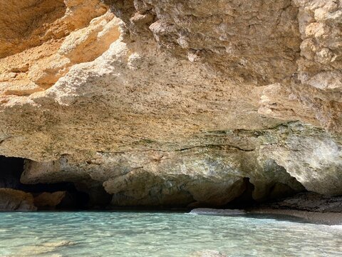 Sea cave in blue lagoon. Beautiful coastal rocks in mysterious grotto. Secluded pebble beach in limestone cliffs. Summer by Mediterranean coast. Paradise laguna landscape.