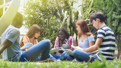 Multi ethnic group of five students sitting on the grass doing homework and relaxing