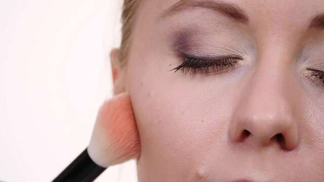 Woman face painting. Makeup artist applying blush bronzer with brush to model cheek. Cosmetic beauty procedures and makeover concept.  Slow motion