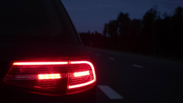 Red tail light of a passenger car parked on the side of the road in the evening. Vehicles with headlights are driving along the motorway. Roadside vehicle designation concept. Copy space for text