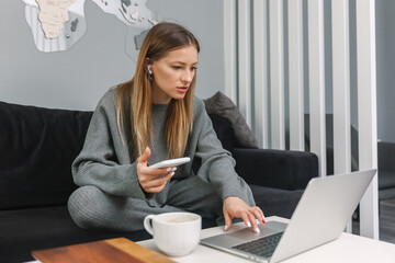 Young woman working on laptop while sitting on sofa at home