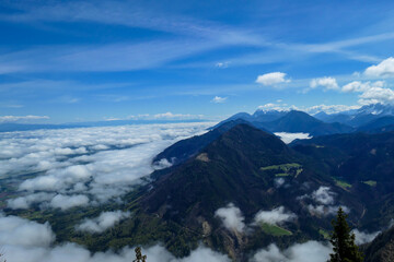 A panoramic view from the top of Alpine peak in Austria. The whole area is shrouded in thick clouds. A few peaks popping out from the clouds. High mountain chains in the back. Carpet from the clouds