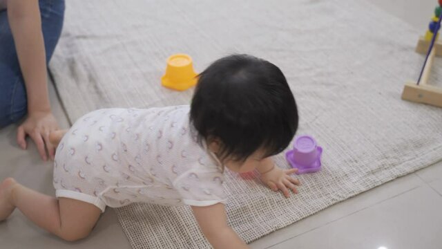 Cropped Shot Curious Baby Girl Eager To Explore Is Crawling Away From Her Mom Who’s Sitting On Knees Near An Armchair And Past Scattered Toys On The Ground.