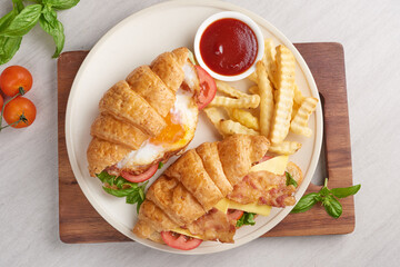 two croissant sandwiches on wooden table, top view, Sandwich with bacon, fried egg. Ham, cheese, bacon, fried egg, tomato, french fries and lettuce served in a plate.